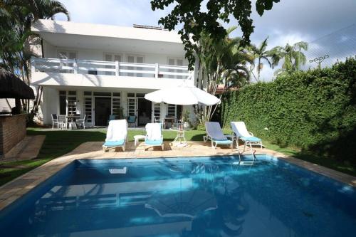 a pool with chairs and an umbrella and a house at Casa em Jardim Acapulco-Guarujá in Guarujá