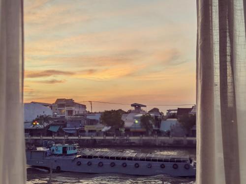 a boat in the water with a sunset in the background at Here Library - A wooden home by the river with a library in Thốt Nốt