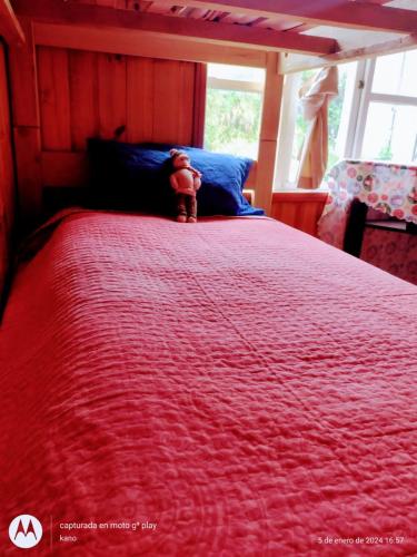 una cama roja con un osito de peluche sentado encima en Hospedaje familiar rural, en Quellón