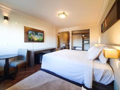 a hotel room with a large white bed and a desk at Suite Confort - Gramado Wish Serrano in Gramado