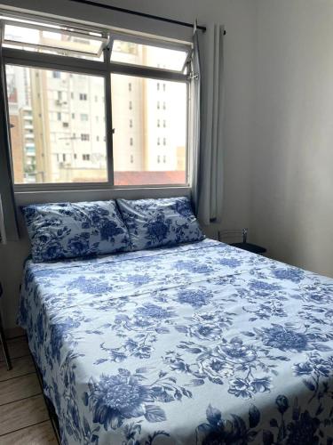 a bedroom with a blue and white bed with a window at Quarto privativo in Balneário Camboriú