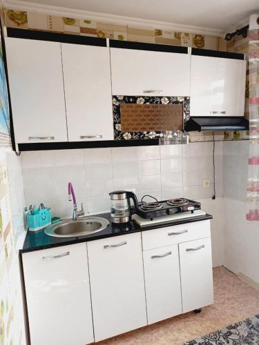 uma cozinha com armários brancos e um lavatório em Medina em Karakol