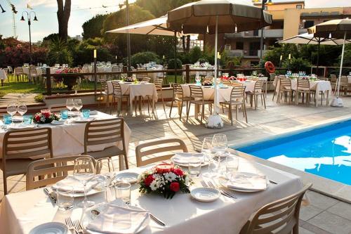 PFA Hotel La Darsena - Follonica في بونتوني دي سكارلينو: طاولة مع طاولات بيضاء وكراسي بجوار حمام سباحة