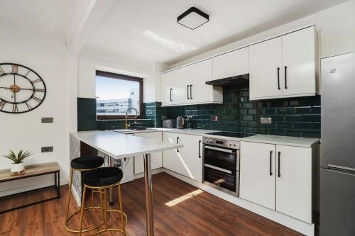 a kitchen with white cabinets and a clock on the wall at New Slick Finnieston Pad w/ Free Parking in Glasgow