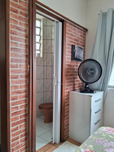 Un dormitorio con una pared de ladrillo y un ventilador en una cómoda en Prático e bem localizado Studio, na CB en Porto Alegre