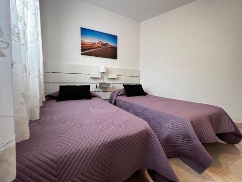 two beds in a room with purple comforter at Precioso y Luminoso Piso in Garachico