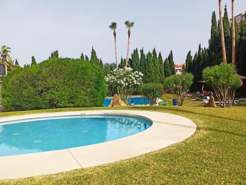 a swimming pool in the middle of a lawn with palm trees at Apartamento Manilva con terraza y piscina in Manilva