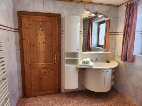 een badkamer met een wastafel, een spiegel en een deur bij Pension Wötzinghof in Kirchberg in Tirol