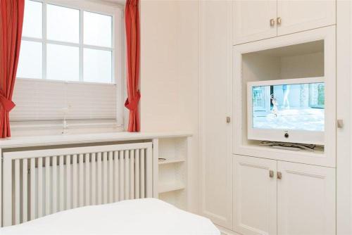 a white bedroom with a tv and a window at Haus-Meerblick in Rantum