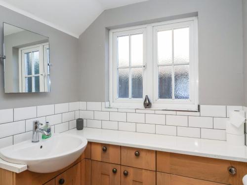 a white bathroom with a sink and two windows at 2 Greensleeves in Saxmundham