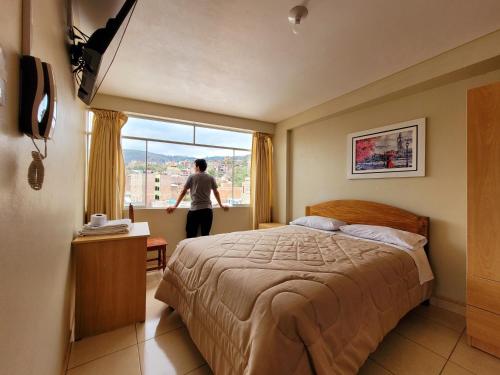 een man in een slaapkamer die uit het raam kijkt bij Illari Wari II-Hotel Sauna in Ayacucho