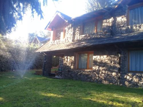 a stone house with a sprinkler in the yard at LA Nevadita, Chalet cabin located near the center- It includes suite room with double bed and another 2 bedrooms with two singles beds- Living room fireplace, Hot water, WI-FI in Villa La Angostura