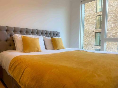 a large bed with yellow pillows and a window at Stunning two bedroom apartment in London