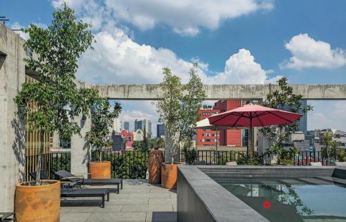 una piscina con ombrellone e sedie rossi e un edificio di Casa Londres by Kukun a Città del Messico