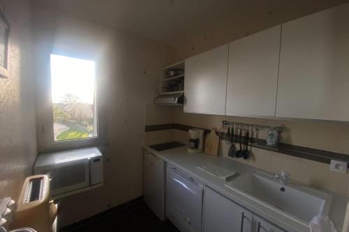 Elle comprend une petite cuisine avec des placards blancs et une fenêtre. dans l'établissement Cozy love cocoon of 34 m direct access to the sea, à Bernières-sur-Mer
