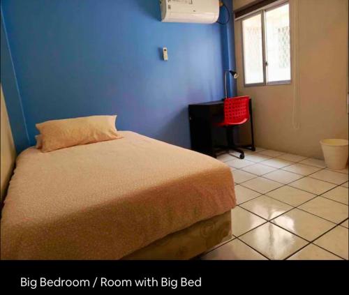 a bedroom with a bed with a blue wall and a red chair at Private Room in Urdesa Central Guayaquil in Guayaquil