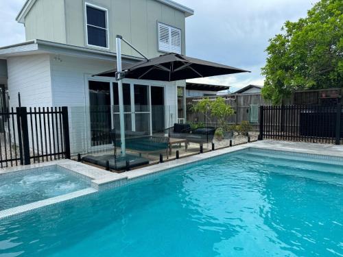 a swimming pool with an umbrella in front of a house at The Beachside Sanctuary -500m from Beach with Pool & Heated Spa in Casuarina