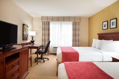 a hotel room with two beds and a desk and a television at Country Inn & Suites by Radisson, Champaign North, IL in Champaign