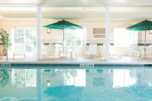 una piscina con sillas, mesas y sombrillas en Country Inn & Suites by Radisson, Rocky Mount, NC, en Rocky Mount