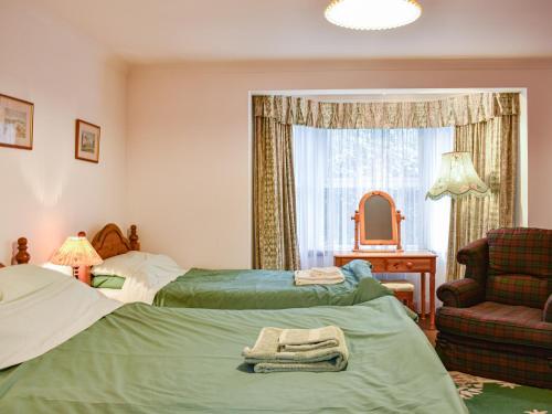 a bedroom with two beds and a chair and a mirror at Pine Tree Cottage - Uk45925 in Ballater