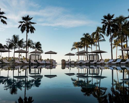 a swimming pool with chairs and umbrellas and palm trees at Four Seasons Resort Oahu at Ko Olina in Kapolei