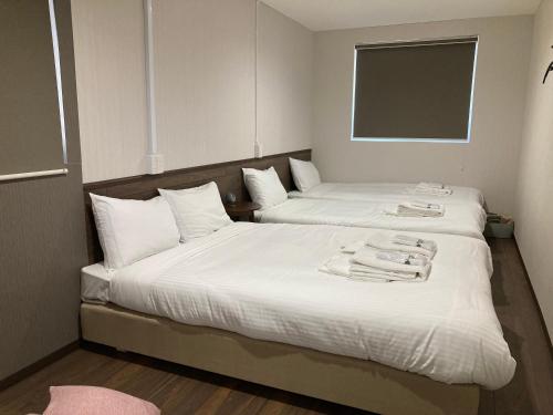 two beds in a room with white sheets and towels at RJ HOTELS OTARU in Otaru