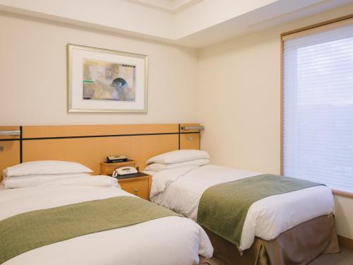 two beds in a room with a window at JR Hotel Clement Takamatsu in Takamatsu