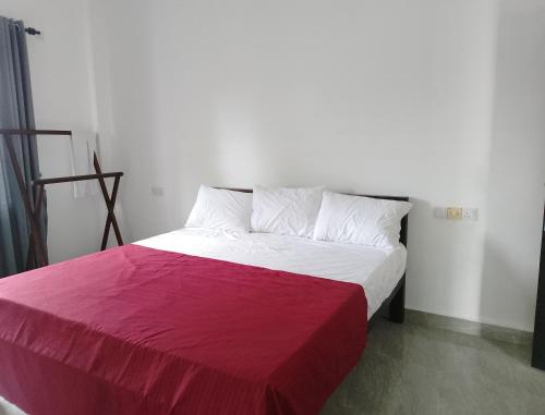 a bed with a red and white blanket on it at Laxsume Guest House Nilaveli in Nilaveli