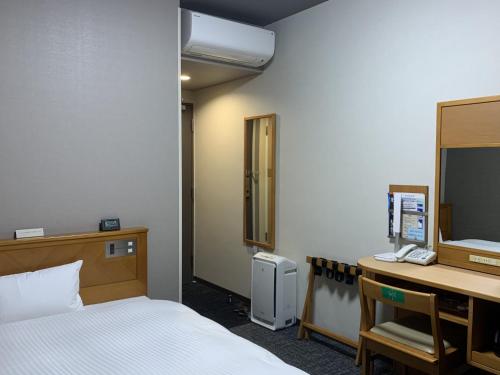 a room with a bed and a desk with a mirror at Hotel Route-Inn Nakatsu Ekimae in Nakatsu