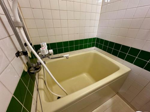 a bath tub in a bathroom with green and white tiles at 1-3サン　地下鉄徒歩圏内サービスアパ―トメントSAPPORO Shiroish iStation エアコンネット完備 in Tsukisappu