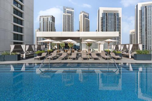 Palace Dubai Creek Harbour في دبي: مسبح الفندق مع الكراسي والمظلات