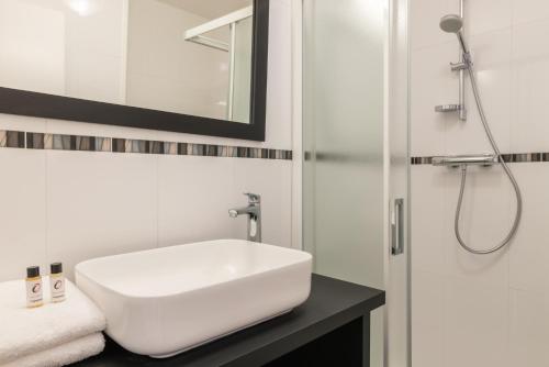 La salle de bains est pourvue d'un lavabo blanc et d'une douche. dans l'établissement Hôtel de Perros, The Originals Boutique, à Perros-Guirec