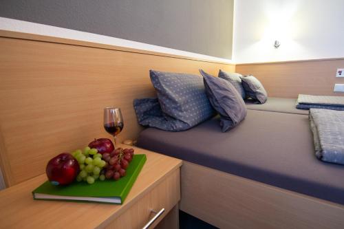 a bed with a plate of fruit and a glass of wine at Green Night Hotel in Falkenstein