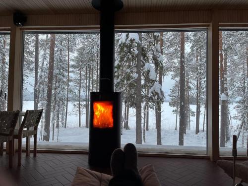 a person is sitting in front of a stove in a room at A unique lakeside cottage in Rovaniemi
