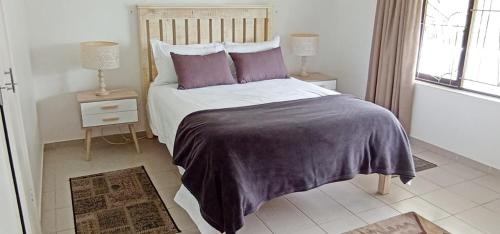ein Schlafzimmer mit einem Bett mit violetter Bettwäsche und einem Fenster in der Unterkunft Pumula on 5th in Pumula