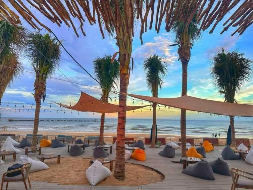 a beach with palm trees and chairs and an umbrella at Novaworld Phan Thiết- 7Days mart in Phan Thiet