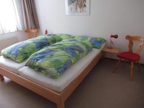 1 cama con sábanas verdes y azules y silla roja en Bot Sundroina (326 Sh) Whg. 2.1, en Lenzerheide