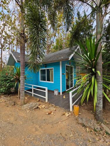 a blue house with a porch and palm trees at Baan Rai Somkiat Homestay Saraburi in Ban Lam Thong Lang
