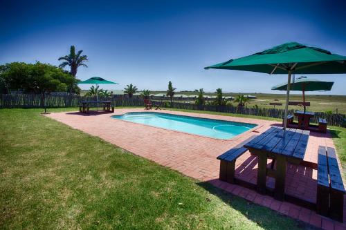 una piscina con sombrilla, mesa de picnic y banco en Mentors Country Estate, en Jeffreys Bay