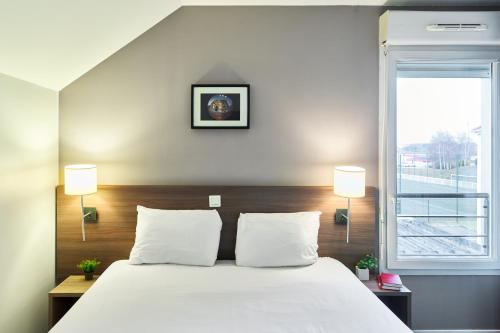 a bedroom with a bed with two lamps and a window at Zenitude Hôtel Résidences Roissy Village in Roissy-en-France