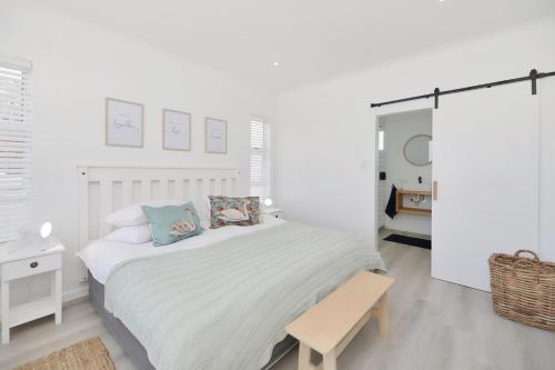 a white bedroom with a bed and a bench at 32 Blouvin Street in Struisbaai