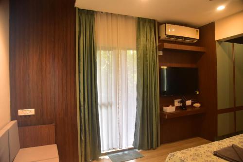 a bedroom with a window with green curtains and a television at UnigoOne- Prime in Canacona