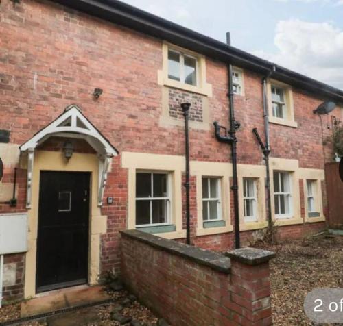 une maison en briques avec une porte noire et un mur en briques dans l'établissement Beautiful Countryside Cottage Alnwick, à Alnwick