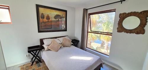 a bedroom with a bed with a mirror and two windows at Laguna Beach K60 - Greenways Golf Estate on Sea in Cape Town