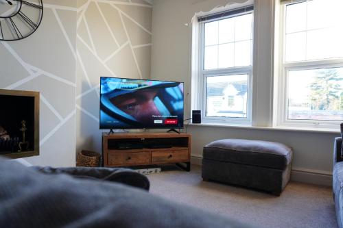 a living room with a flat screen tv and two windows at Heswall apartment in Wirral