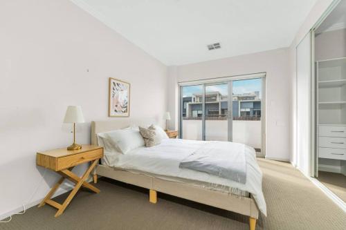 a white bedroom with a bed and a desk and a window at Spacious 3 bed apartment near airport with parking in Sydney