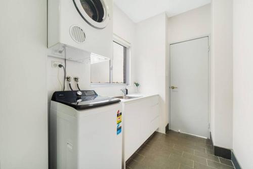 a white kitchen with a sink and a refrigerator at Spacious 3 bed apartment near airport with parking in Sydney