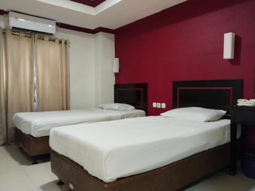 2 camas en una habitación con una pared roja en Metro Hotel Bekasi powered by Cocotel, en Pekayon Satu