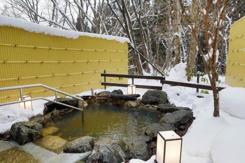 a pool of water in front of a yellow building in the snow at Miyama Ouan Kyoritsu Resort in Takayama
