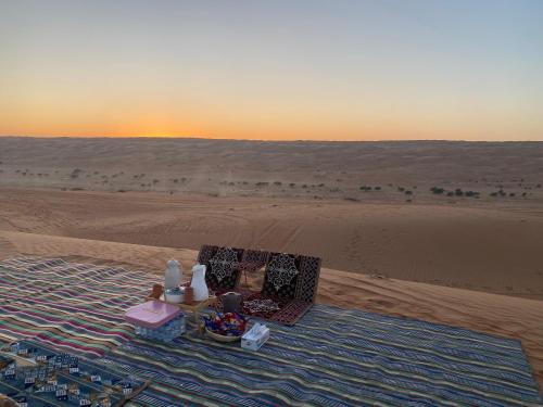 a blanket in the middle of a desert with the sunset at AlRaha Chalet in Bidiyah